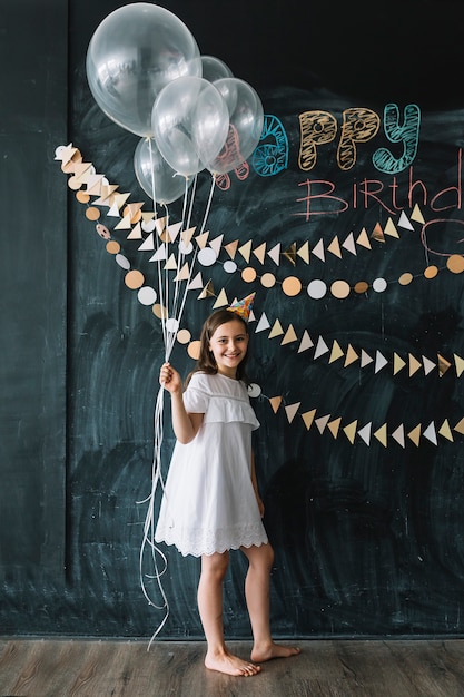 Barefoot girl with balloons near birthday decorations