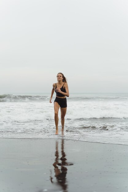 날씬한 몸매를 가진 맨발의 젊은 여성이 몸매를 유지하고 지방을 태우기 위해 수영장 옆 바다 서핑을 하고 있습니다. 푸른 하늘과 해변 배경입니다. 여름 가족과 함께하는 여성 피트니스, 조깅, 스포츠 활동
