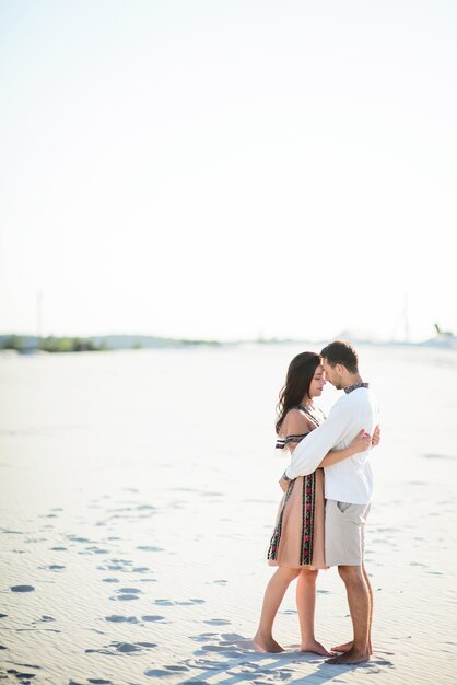 Barefooted couple in bright embroidered clothing hugs tender on a white sand