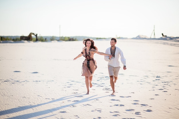 明るい刺繍の衣服を着た裸足のカップルが白い砂の上を走る