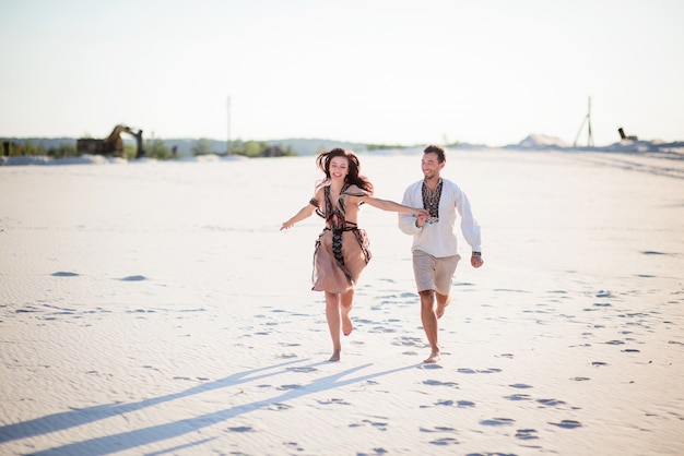 Barefooted couple in bright embroidered clothing runs on a white sand