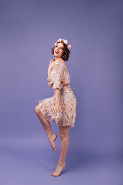 Barefooted girl in romantic summer outfit dancing. Full-length portrait of glad female model with flowers in short wavy hair.