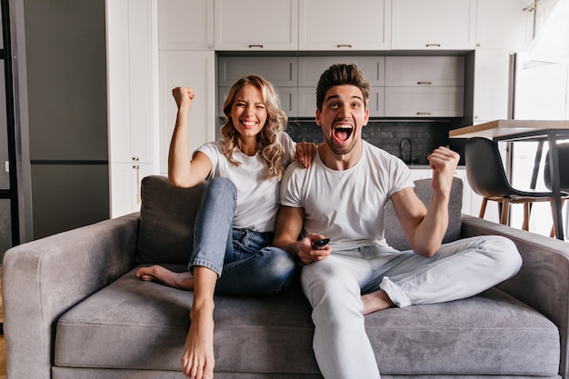 Barefooted girl sitting on sofa with boyriend. Laughing couple watching TV.