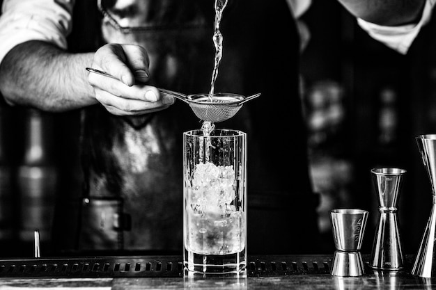 Barista putting alcohol into a cocktail glass with syrup and ice cubes.