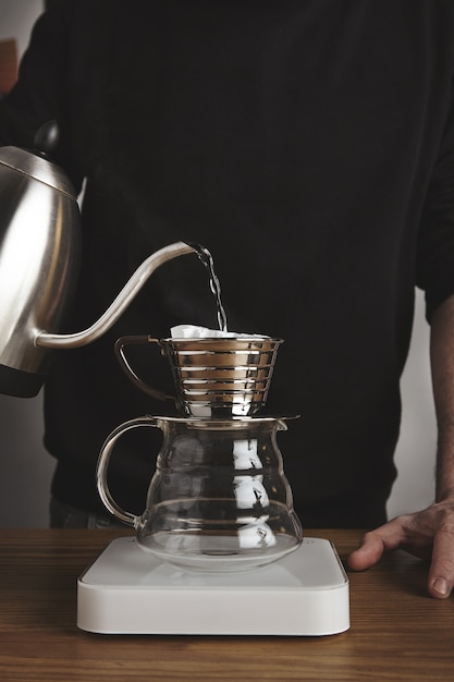 barista spills hot water to prepare filtered coffee from modern teapot to beautiful transparent drip coffee maker on white simple weights.