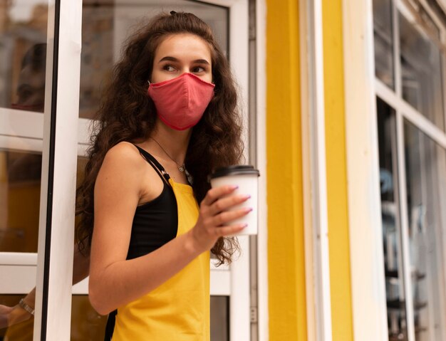 屋外で一杯のコーヒーを保持しながらフェイスマスクを身に着けているバリスタ