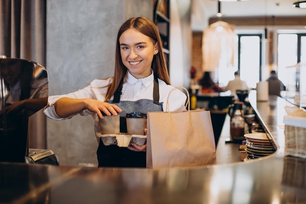 段ボールのカップでコーヒーを準備するコーヒーショップでバリスタの女性