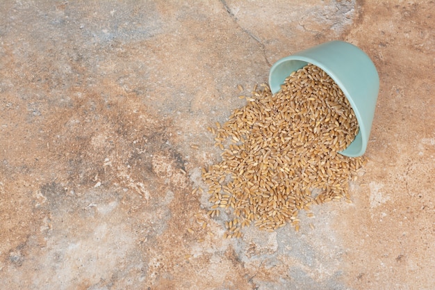 Barley grains out of bowl on marble surface