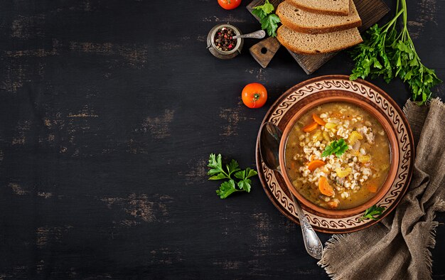 Barley soup with carrots, tomato, celery and meat on a dark background. Top view.
