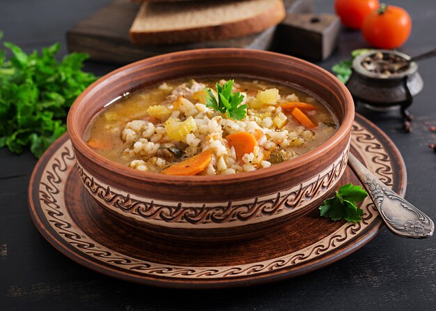 Barley soup with carrots, tomato, celery and meat on a dark surface