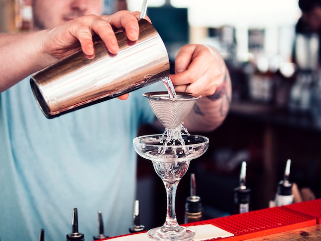 Barman filling cocktail glass with alcohol beverage