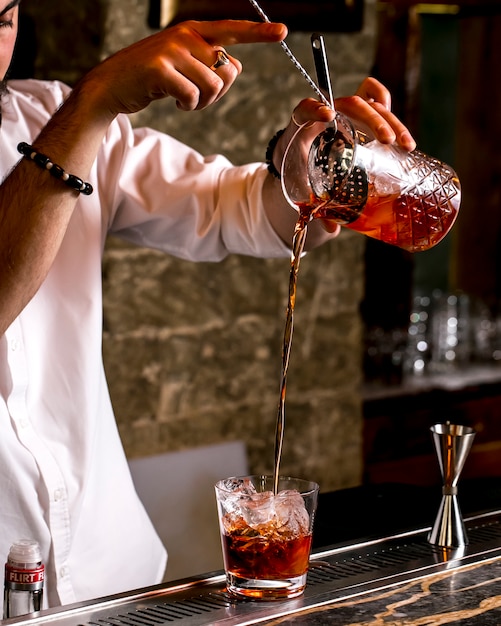 Free photo barman pours cocktail through cocktail strainer