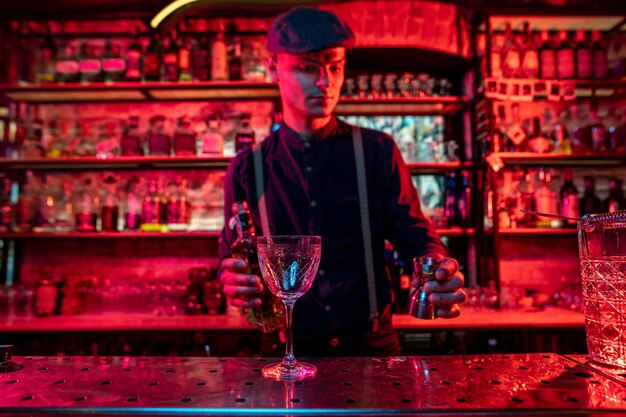 Barman preparing the alcoholic cocktail in multicolored neon light, focus on glass