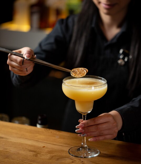 Bartender adding lemon slices into orange cocktail.