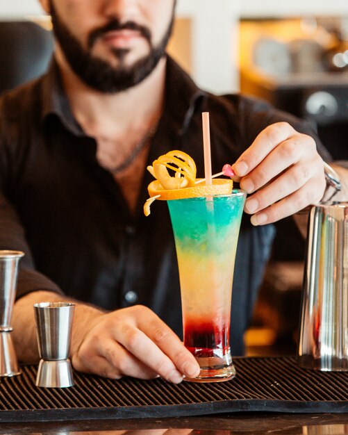 Bartender decorates colorful cocktail with orange zest