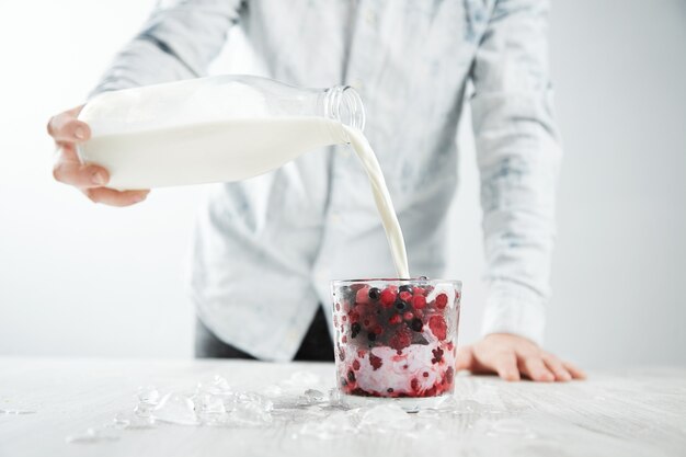 Bartender man pours milk from vintage bottle to glass with milky shake cocktail with frozen berries