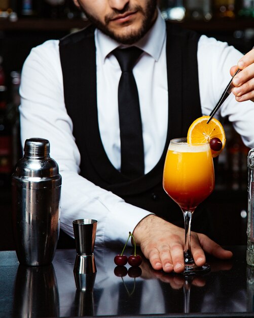 Bartender places orage slice on cocktail