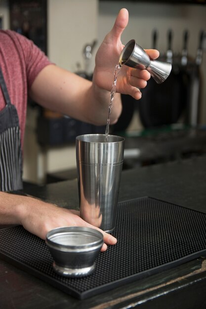 Bartender pouring cocktail in shaker at bar counter