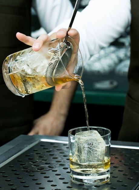 Bartender pours a drink into a glass with lots of ice