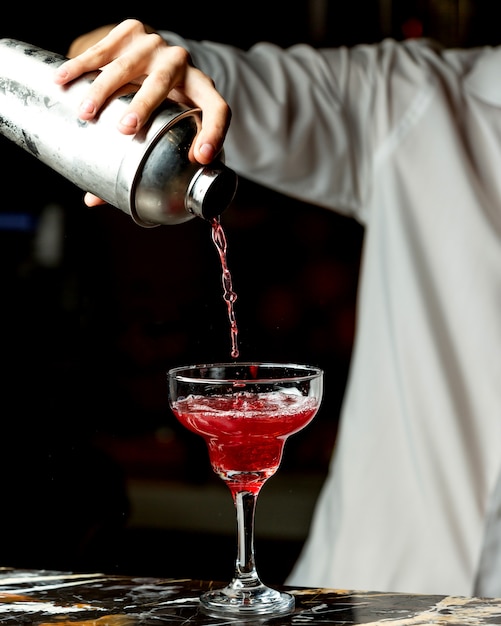Bartender pours red cocktail into a glass with long stem