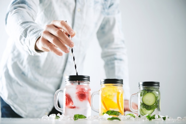 Free photo bartender puts striped drinking straw in jar with fresh cold homemade lemonade made from ice, strawberry, orange, cucumber and mint.