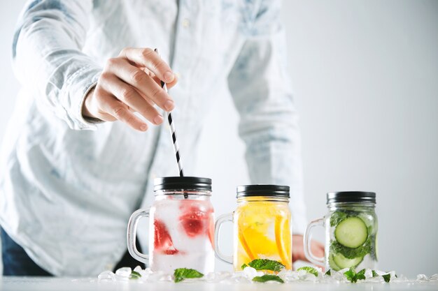 Bartender puts striped drinking straw in jar with fresh cold homemade lemonade made from ice, strawberry, orange, cucumber and mint.