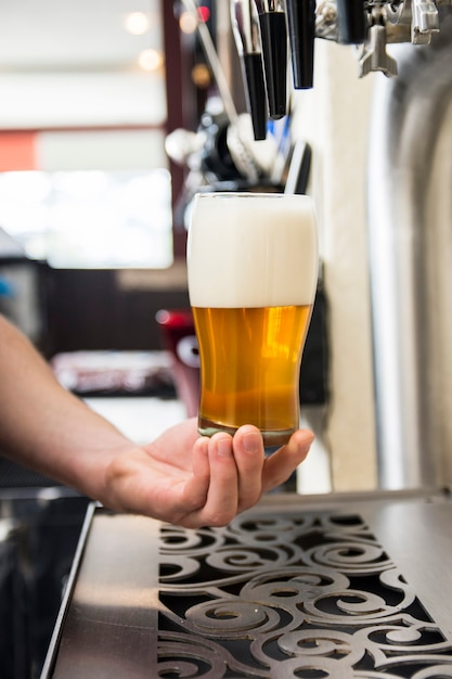 Bartender's hand holding large beer glass under the tab