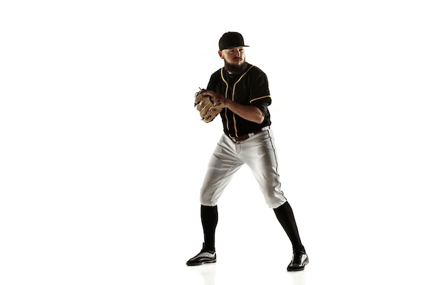 Baseball player, pitcher in a black uniform practicing and training isolated on a white wall. Young professional sportsman in action and motion. Healthy lifestyle, sport, movement concept.