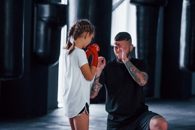 Основные удары. молодой татуированный тренер по боксу учит милую девочку в тренажерном зале.