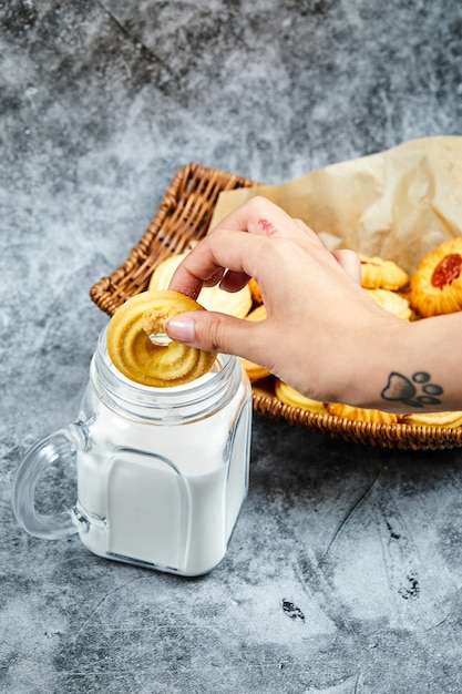 Basket of assorted biscuits, milk and hand holding a biscuit.