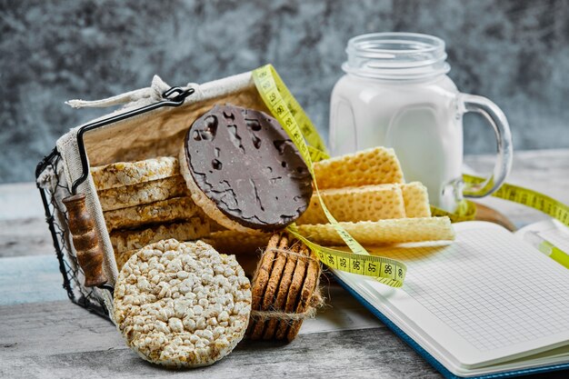 Basket of biscuits and a jar of milk on a wooden table with a notebook.