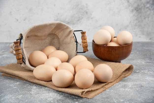 Basket and bowl full of organic fresh uncooked eggs on marble surface.