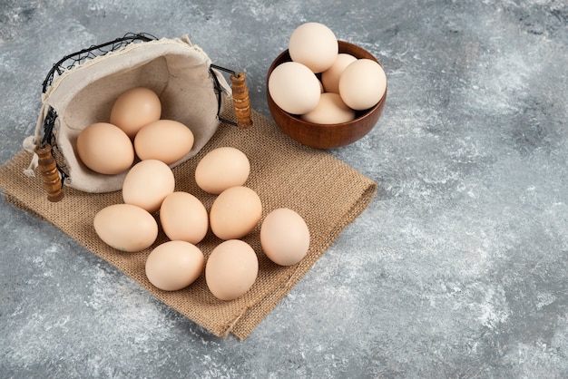 Basket and bowl full of organic fresh uncooked eggs on marble surface.