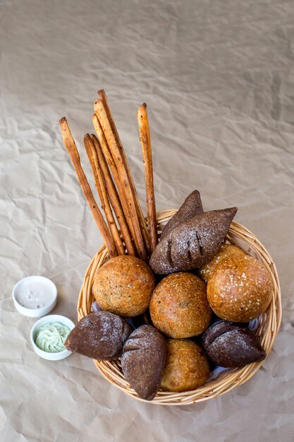 A basket of bread buns with brown, spicy breads and bread sticks