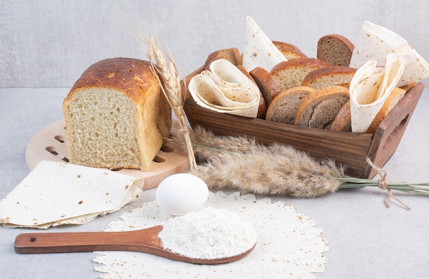 Basket of bread and lavash on table with egg and flour