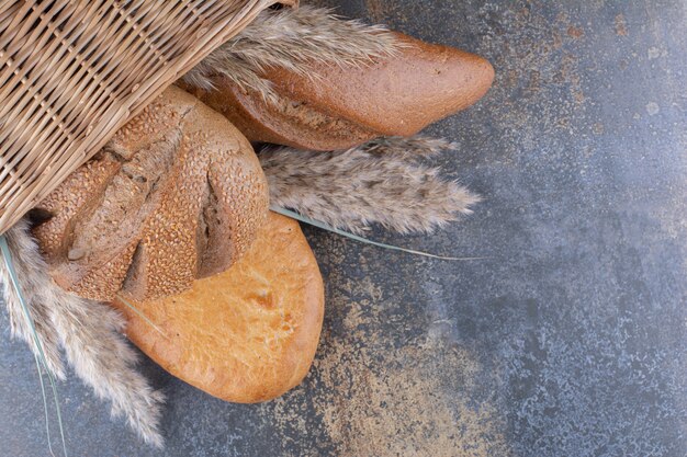 Basket of bread loaves and feather grass stalks on marble surface