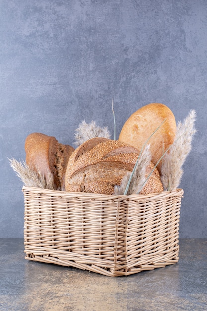 Basket filled with bread loaves and feather grass stalks on marble surface