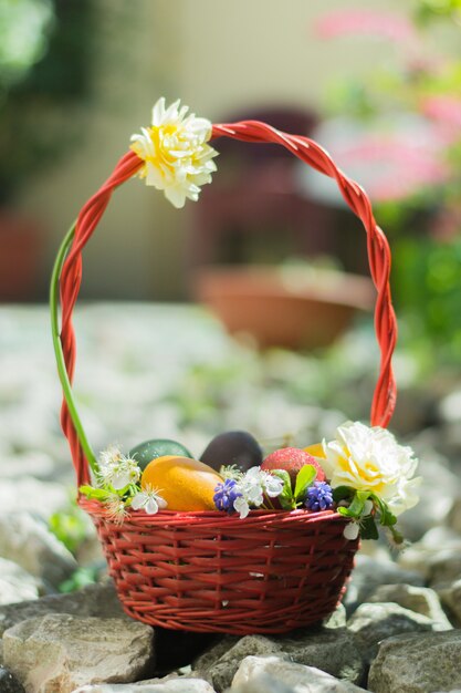 Basket filled with colorful easter eggs and decorated with white flowers on the rocks