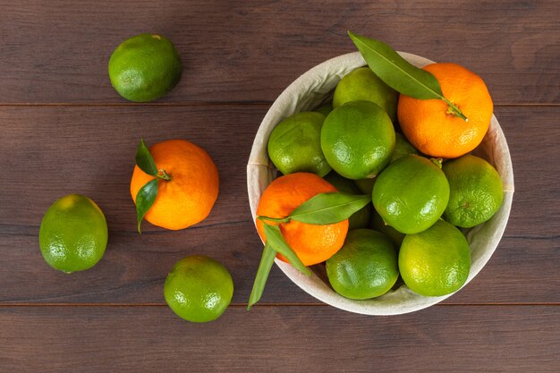 корзина с зелеными лимонами и апельсинами на коричневой деревянной поверхности