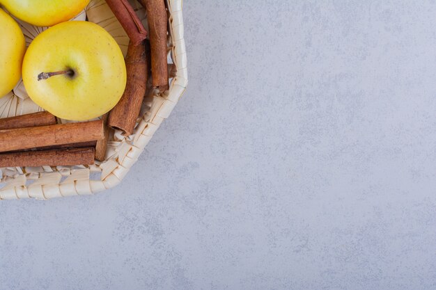 Basket full of cinnamon sticks and apples on stone table. 