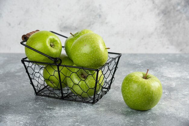 大理石のテーブルの上の緑の光沢のあるリンゴでいっぱいのバスケット。