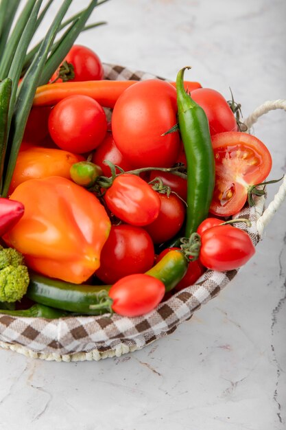 Basket full of vegetables as tomatoes, peppers and scallions on white surface