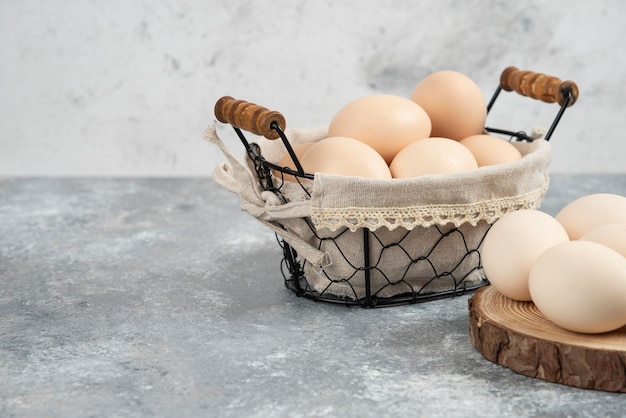 Basket of organic fresh uncooked eggs placed on marble surface.