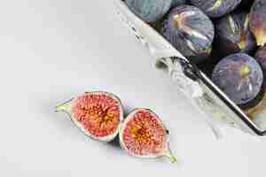 Free photo a basket of purple figs on white with slices of fig aside.