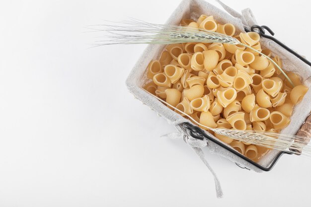 Basket of raw pasta with ears of wheat on white.