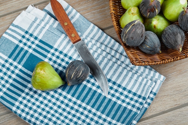 A basket of ripe figs on wooden table next to knife and a tablecloth.