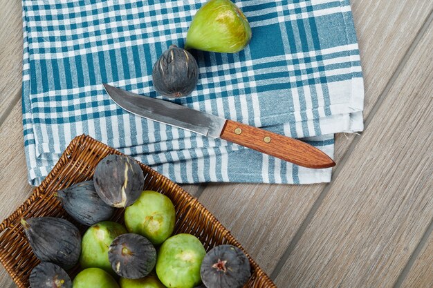 A basket of ripe figs on wooden table with a knife and a tablecloth.