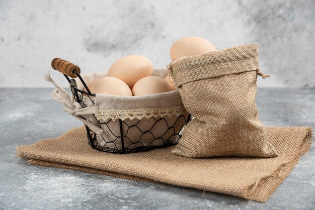 Basket and sackcloth of organic fresh uncooked eggs on marble surface.