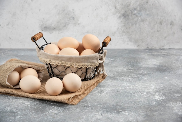 Foto gratuita cestino e tela di sacco di uova crude fresche organiche sulla superficie di marmo.
