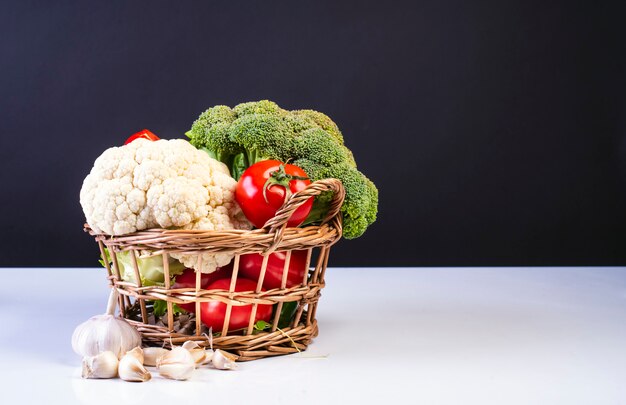 Basket of tomatoes, broccoli and cauliflower on white surface and black surface